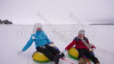 快乐的妈妈和女儿在冬天的雪中雪橇，玩雪球。 母亲和孩子笑着快乐地滑行