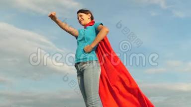 女孩梦想成为超级英雄对抗蓝天。 站在红色斗篷里的年轻女孩表达了梦想。 美丽美丽