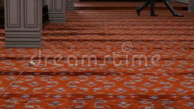一个大的灰色吸尘器清洁地毯。 伊斯坦布尔，一个人在蓝色清真寺里吸了一块巨大的红地毯