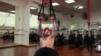 美丽的，肌肉发达的运动男子收紧在悬挂的绳索，增加肌肉。