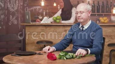 一位悲伤的老人坐在餐厅的桌子旁等待他的约会