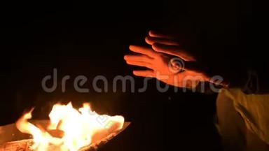 一个人在完全的黑暗中把手放在明火上取暖。 男人`夜晚的炉火旁