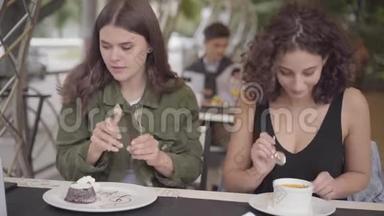 两个年轻女朋友坐在户外咖啡馆里吃蛋糕的肖像。 年轻女孩一起<strong>享用美食</strong>
