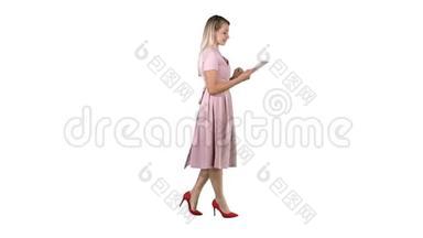 金发碧眼，穿着粉色连衣裙，走路，在白色背景上使用平板电脑。
