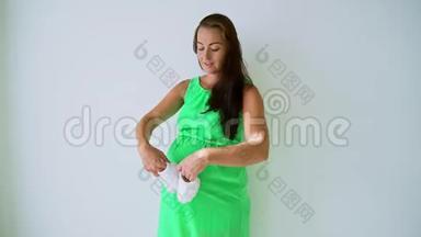 穿着内衣的怀孕妈妈在玩婴儿鞋。 带带的肚皮
