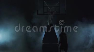 健康的年轻人在黑色背景下和烟雾一起打篮球。 穿着红色衬衫和黑色短裤。