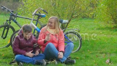 坐在草地上玩智能手机的男孩。 妈妈带儿子`智能手机