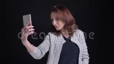 一张中年黑发白种女人用黑色背景的智能手机自拍的照片。