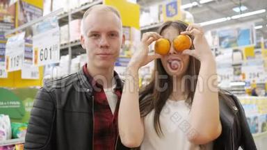 在超市的年轻夫妇。 女孩在做滑稽的鬼脸，橘子在超市里看着相机。