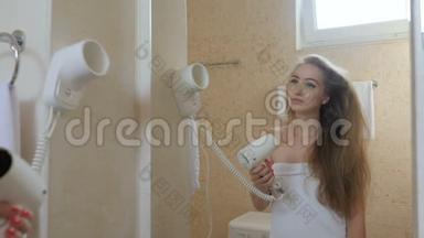 穿着浴巾的漂亮女孩在浴室里用吹风机