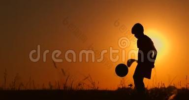 一个男孩在海滩上踢足球或踢足球的剪影，背景是美丽的日落