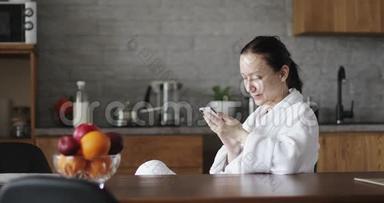 一个穿着<strong>白色浴袍</strong>的成年女人正在手机上输入一条信息。