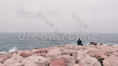 孤独悲伤的人坐在靠近海洋的大石头上。 上班族每天下班后坐在海边。 孤独的男孩望着大海。