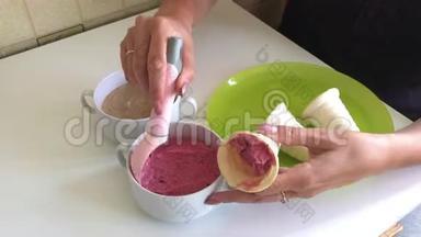 一个女人把草莓冰淇淋装满了喇叭。 用冰淇淋勺。 放在盘子上。 桌子上有集装箱和
