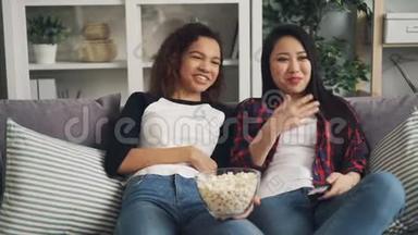 非裔美国人和亚裔女青年在家里享受电视上的喜剧，笑、说、吃爆米花，放松<strong>身心</strong>