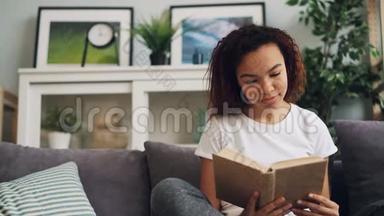 一个美籍非洲裔学生正在看<strong>书</strong>，面带微笑，然后独自坐在舒适的沙发上<strong>翻页</strong>