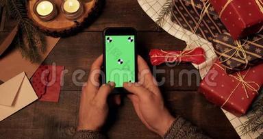 木制圣诞装饰<strong>桌子</strong>上全新智能手机垂直绿色屏幕上的手敲击的<strong>俯视</strong>图