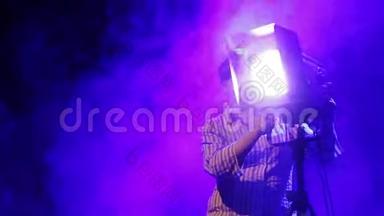 舞台上的一位年轻女子照明器在烟雾中用一台戏剧轮廓<strong>投影</strong>仪工作。
