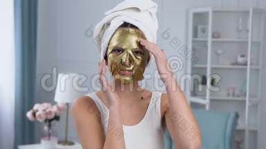 英俊的微笑女人在脸上固定恢复活力的化妆品金色组织面具的肖像。