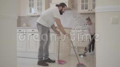 爸爸留着胡子，小可爱的女儿用扫帚和簸箕在新的现代化厨房里打扫卫生