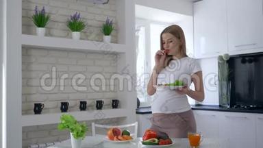 怀孕期间的营养和饮食，女人手里拿着一盘沙拉，吃着甜椒，抚摸着肚子