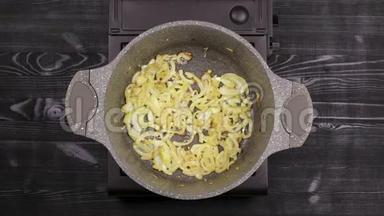 切片洋葱片在平底锅中烤，用大理石或石头不粘涂层涂成金黄色。 石油在b上沸腾