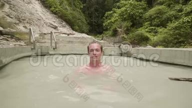年轻人在户外水疗中心享受热浴。 帅哥在矿泉水池里洗澡。 天然水疗中心