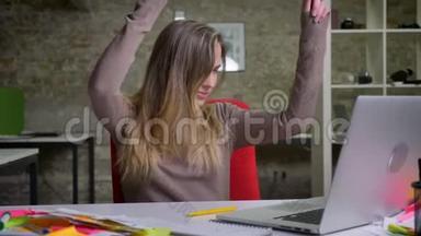 漂亮的白种人女办公室工作人员坐在笔记本电脑前快乐跳舞的特写镜头