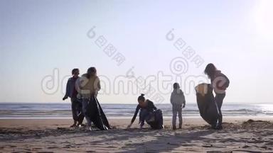 女孩志愿者清理海岸线的垃圾。妇女们把冲上岸的垃圾装在黑色的袋子里。生态
