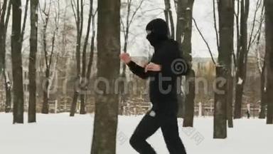 一个穿着黑色运动服和巴拉克拉瓦的年轻人，在一个冰雪覆盖的城市训练前做热身运动