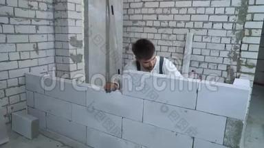 年轻的白种人建筑工人检查泡沫水平的新建墙体的均匀度