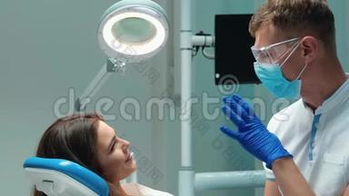 年轻英俊的牙医，戴着医用蓝色手套、口罩和眼镜，与美丽的病人讨论过程