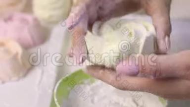 一个女人在糖霜中以玫瑰的形式卷棉花糖。 桌子表面附近有一个现成的棉花糖