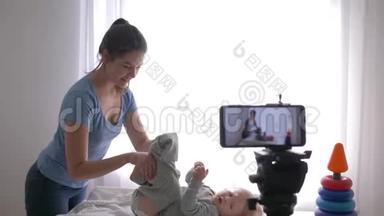 博客职业，现代母亲vlogger在手机上录制训练视频时，为小男孩换衣服