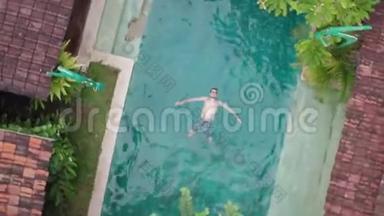 在蓝泳池上漂浮的年轻人在热带地区享受日光浴和度假的无人机鸟瞰