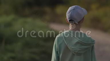 一个戴帽子的男孩在户外的乡间小路上散步