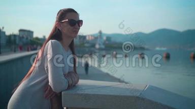 夏天天气晴朗，戴太阳镜的年轻迷人女孩。 一个女孩站在靠近大海的堤岸上..