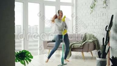 快乐的家庭主妇在打扫房间时跳舞唱歌，她用耳机听音乐，拖地板