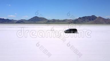 无人机跟随现代小型货车沿着平坦盐湖沙漠的大气景观进行完美的美国公路旅行。