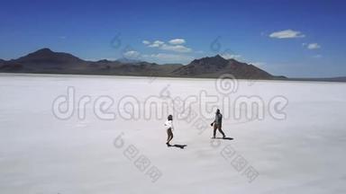 在史诗般的盐湖沙漠景观中，兴奋的浪漫情侣一起散步，拥抱在一起的电影航拍镜头。