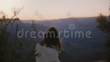 慢镜头后景，快乐宁静的年轻女子，飞扬的头发，坐着观看史诗般的日落，俯瞰大峡谷全景。