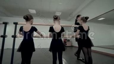 舞蹈班的黑发女老师向穿着黑色紧身衣的芭蕾舞女演员展示如何站在芭蕾舞附近