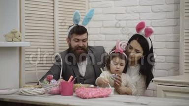 母亲、父亲和女儿正在画复活节彩蛋。 幸福的家庭正在为复活节做准备。 可爱的小女孩