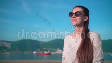夏天<strong>天气晴朗</strong>，戴太阳镜的年轻迷人女孩。 女孩坐在靠近大海的堤岸上..