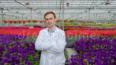 一位年轻的男科学家或农学家，穿着一件白色外套，在温室里放着花的床的背景下工作