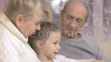祖父和祖母正在读一本书，他们的孙女坐在家里的沙发上，家庭价值观