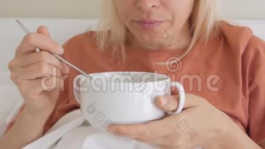 一个女人，一张悲伤痛苦的脸，坐在白色毯子下的床上，吃着一盘汤。