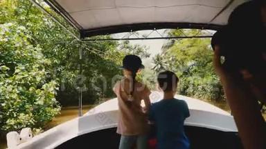 小快乐的女孩和男孩一起在狩猎之旅船上沿着异国情调的丛林河航行，年轻的女人为他们拍照。