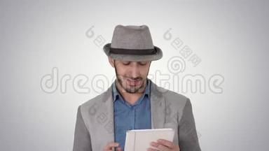 英俊的微笑阿拉伯男子戴着帽子走路和使用平板电脑的梯度背景。