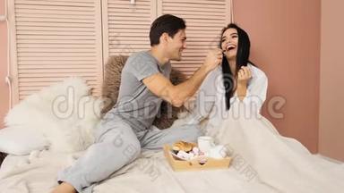 爱的夫妇在酒店的床上吃早餐，互相喂食。 慢动作